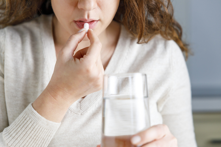 Cropped shot of young woman taking pill holding a glass of water in the kitchen