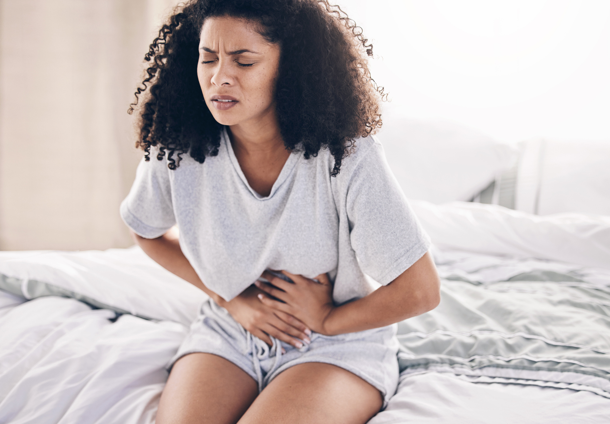 Abdomen pain, period and black woman in bed with abdominal cramps, menstruation and stomach ache. Health, medical emergency and girl with digestion problem, pms crisis and endometriosis in bedroom