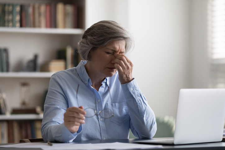 Tired middle aged woman taking off eyeglasses, suffering from painful feelings or having blurry eyesight, having astigmatism problem. Stressed due to long computer workday old lady relieving eyes pain