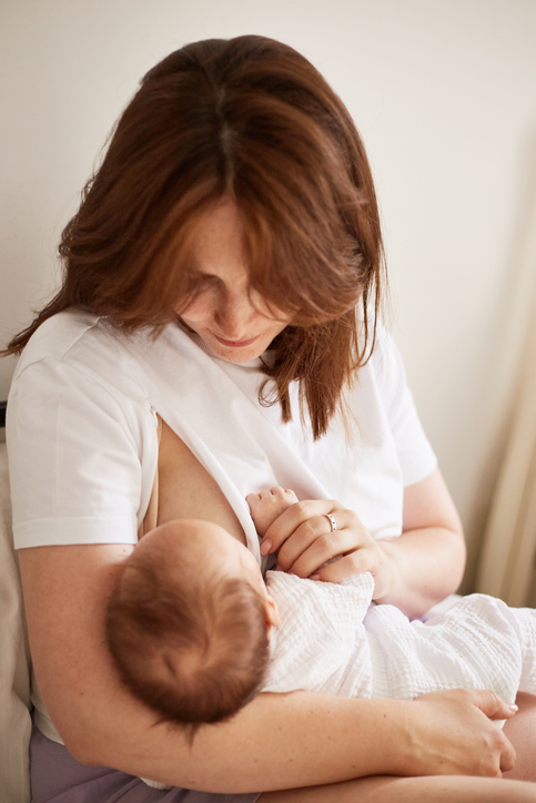Mother breastfeeding her newborn baby boy. Realistic home portrait