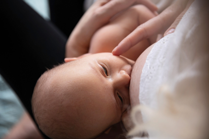 Caucasian european white mother breastfeeding her newborn baby, at home or hospital. Baby in detail, mother s face is not visible, only the child. With eyes open, being latched. Very discreet photo of a link, bond, caring and best nutrition for young child.