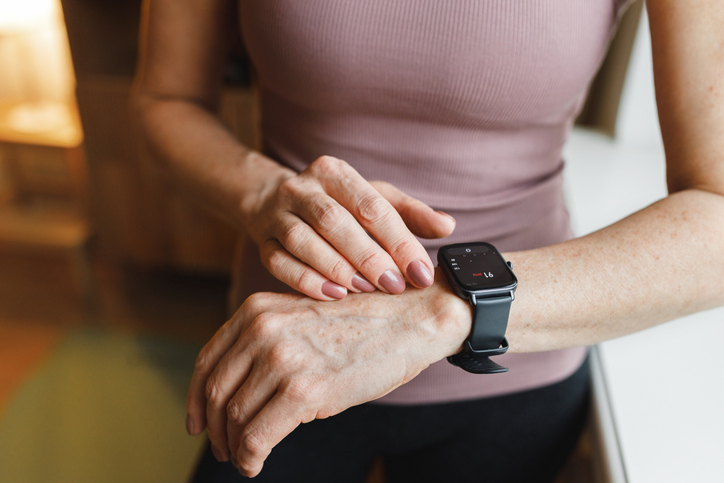 Closeup cropped image of hands of middle-aged woman adjusting or checking fitness tracker or health data as distance, heart rate, lost calories on smartwatch after morning run outside