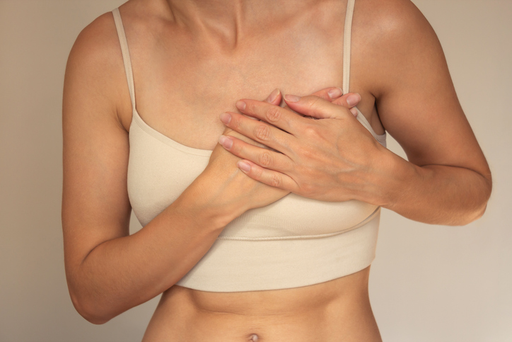 A young woman in beige underwear holds the left side of her chest with both hands from pain, suffers from arrhythmia, difficulty breathing, panic attacks. Women's health