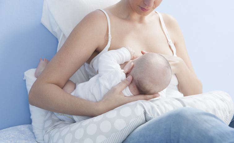 Young mother feeding breast. She is using a nursing pillow with the baby on side
